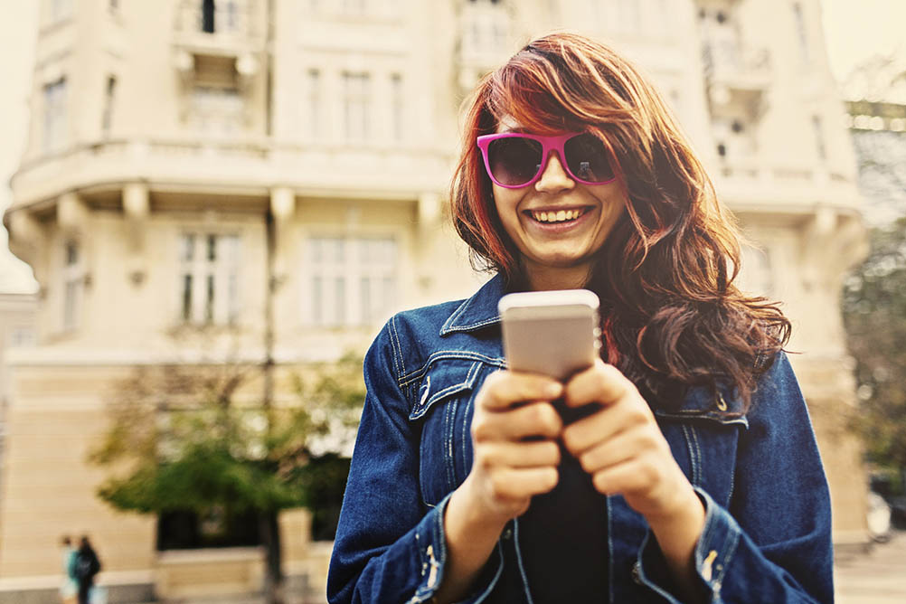 Smiling young woman holds her phone in front of her 