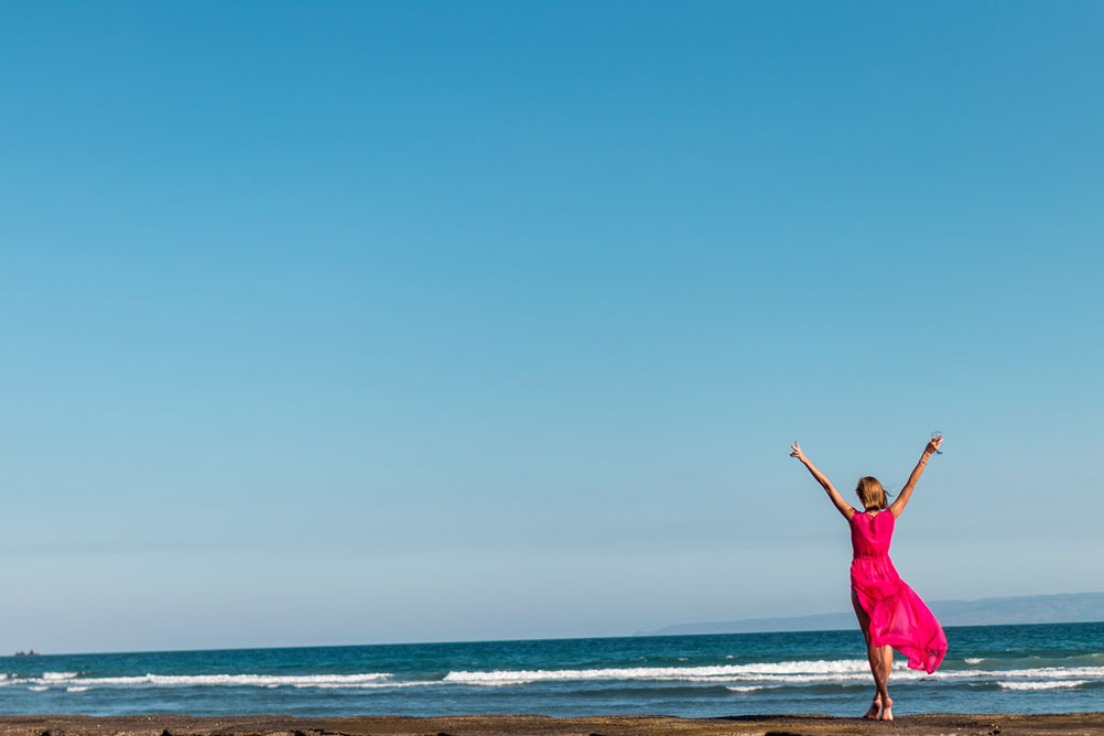 A woman celebrates a lottery win next to the sea against a blue-sky background