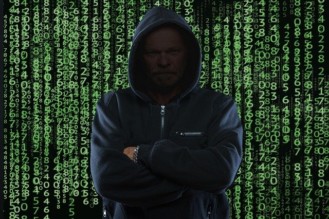 A hooded hacker stands in front of a wall of data