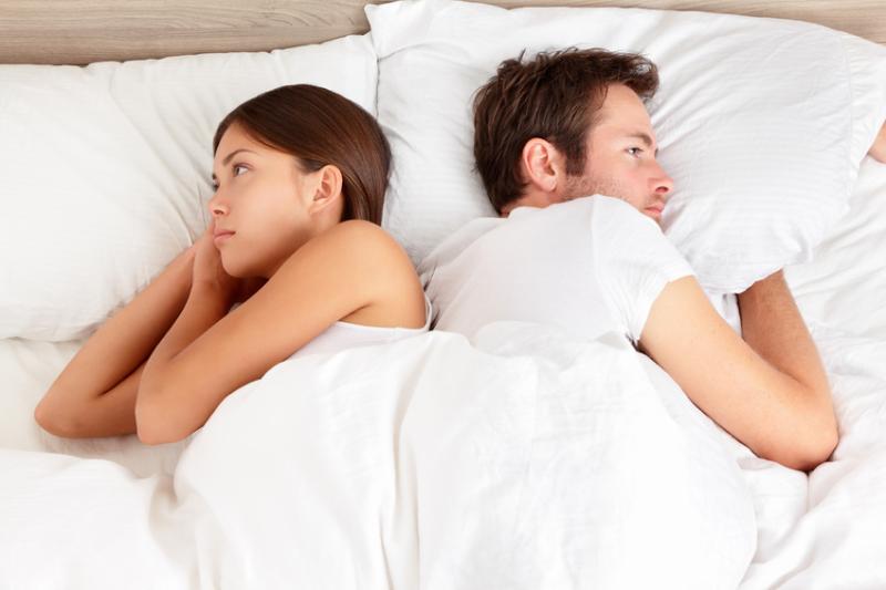 Unhappy couple lie in bed facing in opposite directions